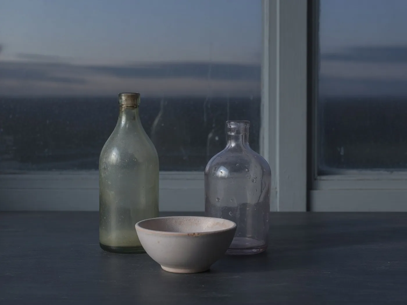 Two glass bottles and a small bowl against a dusk window