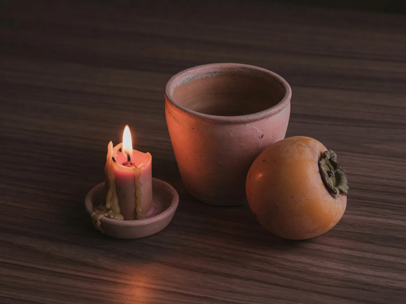 A candle, a clay pot, and a persimmon in warm low light