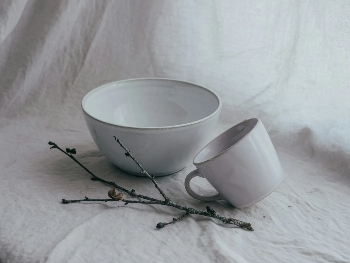 A white bowl, a pale cup, and a winter twig on linen